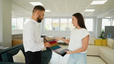 Bir müşteri mobilya danışmanıyla çeşitli kumaş örneklerini gözden geçirir. Mobilya mağazasında ev dekorasyonu için mükemmel rengi ve dokuyu bulmayı amaçlar.