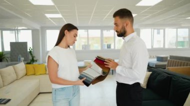 Bir müşteri ve danışman kumaş seçeneklerini gözden geçirir, kendi tarzına ve ihtiyaçlarına uygun kişiselleştirilmiş bir kanepe yaratmak için renkleri ve dokuları dikkatlice düşünür.
