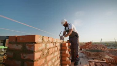 Hintli bir müteahhit, güneşli bir günde modern bir binanın inşaatı sırasında ustalıkla tuğla bir duvarda çalışır.