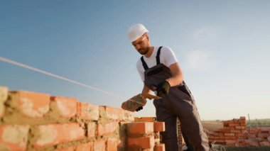 Odaklanmış bir müteahhit, temiz gökyüzünün altında güçlü bir yapı sağlamak için hassas bir tuğla yerleştirir. Güneşli bir inşaat gününde kendini zanaatkarlığa adamış.