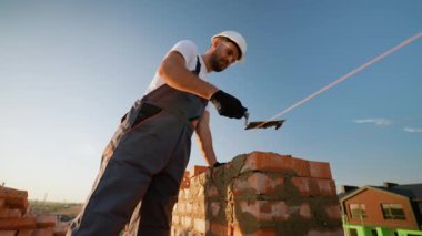 Yetenekli bir inşaatçı, çağdaş bir konut kompleksi için tuğla döşeyerek özenle çalışır. Hassasiyet ve uzmanlık modern konut vizyonunu hayata geçiriyor