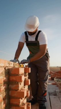 Odaklanmış bir müteahhit, temiz gökyüzünün altında güçlü bir yapı sağlamak için hassas bir tuğla yerleştirir. Güneşli bir inşaat gününde kendini zanaatkarlığa adamış.
