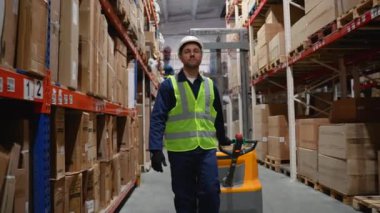 Dolu ve verimli bir depoda depo koridorlarında ilerlerken güvenlik yeleği ve forklift kullanan bir depo çalışanı.