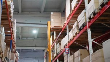 Bir forklift, lojistik ve depolama işlemlerinde hassasiyet ve verimliliği gösteren büyük bir kutuyu bir depodaki en üst raftan dikkatlice kaldırır.