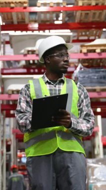 Afro-Amerikan depocu, pano teslimatı yapıyor, depoda stokları var. Depo çalışanı malları nakliyeye hazırlıyor.