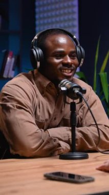 Kulaklık takan Afrikalı Amerikalı blogcu, profesyonel ekipmanlarla modern bir stüdyoda radyo podcast kayıt oturumunda görüşlerini paylaşıyor.