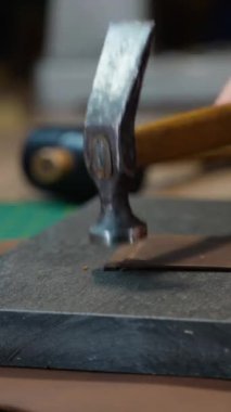 Deri üzerinde çalışmak için çekiç kullanan bir zanaatkârın yakın çekimi, yüksek kaliteli bir deri ürün üretmede beceri ve özen gösteriyor