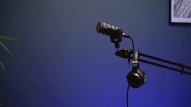 Modern bir podcast stüdyosunda profesyonel bir mikrofon ve kulaklığın yakın çekimi. Minimalist tasarım ve mavi ışık sakin bir atmosfer yaratır.