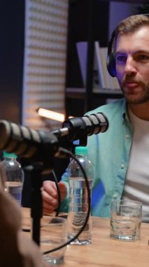 Tutkulu bir podcast sunucusu, modern bir stüdyoda canlı ve ilgi çekici bir konuşma yaratarak, bir kayıt sırasında bir konukla canlı bir şekilde etkileşime geçiyor.