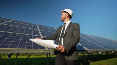Zırhlı bir mühendis elinde planlar, güneşli bir alanda güneş paneli kurulumunu denetliyor temiz ve sürdürülebilir yeşil enerjiyi sembolize ediyor.