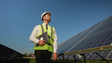 Kurulumdan sonra güneş enerjisi santralinde yürüyen takım elbiseli bir mühendis, sürdürülebilir enerji üretimi için her şeyin hazır olduğundan emin oluyor.