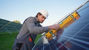 Adanmış bir işçi, sürdürülebilir enerji üretimi için performansı optimize ederek, güneş panellerinin doğru kurulumunu sağlamak için hassas seviye bir araç kullanır