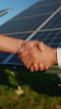 Güneş panelleri önünde el sıkışan iki profesyonelin yakın çekimi, yenilenebilir enerji projesinde başarılı bir işbirliği ve anlaşmayı sembolize ediyor