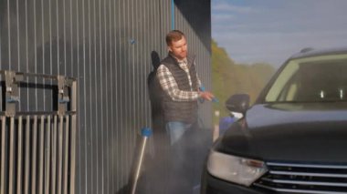 Açık hava oto yıkama servisinde arabasını temizlemek için yüksek basınçlı hortum kullanan bir adam modern bir tesis ile gün ışığında kusursuz bir temizlik sağlıyor.