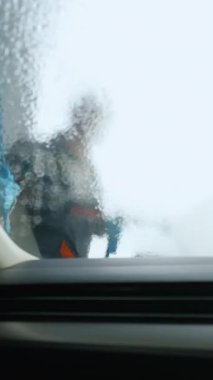 Araba yıkama işçisi ön cama köpük sürerken, camda köpüklü, köpüklü bir sabun tabakası oluşturarak temizleme işlemi yaparken içeriden görüntüyü alın.