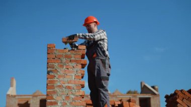Güvenlik teçhizatı kullanan bir inşaat işçisi, konak inşa ederken binaların kalitesini sağlamak için tuğlaları titizlikle yerleştirir.
