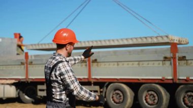 Başlık takan bir inşaat ustası vinç tarafından kaldırılan beton levhanın yerini belirliyor. İnşaat alanında hassas takım çalışması.