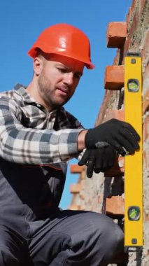 Güvenlik kaskı takan bir inşaat işçisi, düz bir alet kullanarak tuğla duvarın doğruluğunu garanti altına alır. Hassasiyet ve adanmışlık vurgulandı