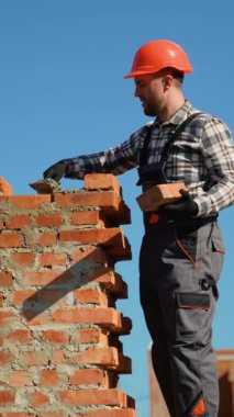 Güvenlik kaskı takmış kendini adamış bir inşaat işçisi iki katlı bir konak inşa ediyor.