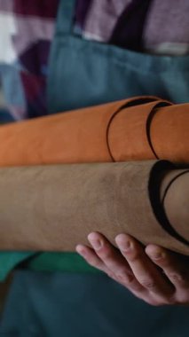 Bir zanaatkar, yüksek kaliteli el yapımı deri ürünler için hammaddeleri sergilerken, çeşitli toprak tonlarında yuvarlanmış deri taşır.