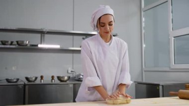 Beyaz üniformalı bir kadın şef, profesyonel bir mutfakta ahşap bir masaya hamur yoğurur. Pişirmeye ya da pişirmeye hazırlanır..