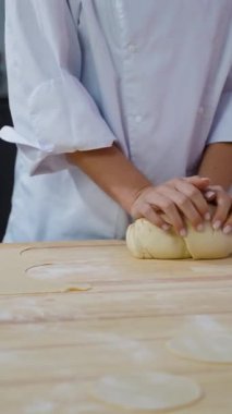 Beyaz üniformalı bir kadın şef, profesyonel bir mutfakta ahşap bir masaya hamur yoğurur. Pişirmeye ya da pişirmeye hazırlanır..