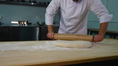 Profesyonel bir aşçının, mutfaktaki un kaplı bir yüzey üzerindeki hamuru düzleştirmek için ahşap bir oklamalı iğne kullandığı yakın plan..