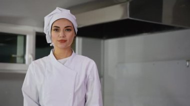 Beyaz üniformalı ve aşçı şapkalı bir kadın aşçının yakın çekimi modern bir profesyonel mutfak ortamında güven içinde poz veriyor..