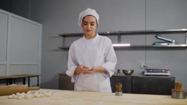 Modern bir mutfak ortamında ahşap bir çalışma masasında taze hamur köftelerini elle katlayan profesyonel bir şef..