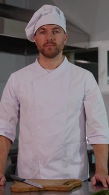 Beyaz üniformalı ve şapkalı bir şef modern ekipman ve aletlerle profesyonel bir mutfakta güvenle duruyor.
