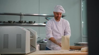 Profesyonel bir aşçının yakın plan resmi. Ticari bir mutfaktaki hamur kesme makinesinden düzleştirilmiş hamur tabakasını dikkatlice çıkarıyor.