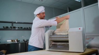 Üniformalı profesyonel bir aşçı hazır olmak için hamur kesme makinesine hamur koyuyor..