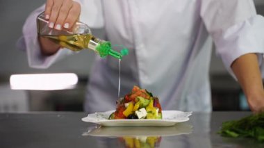 Şefin ellerinin renkli bir sebze salatasının üzerine zeytinyağı dökerek sağlıklı bir yemek hazırladığı yakın çekim..