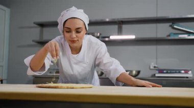 Beyaz üniformalı odaklanmış bir şef, profesyonel bir mutfakta, ahşap tezgahın üzerine peynir serpiştiriyor..