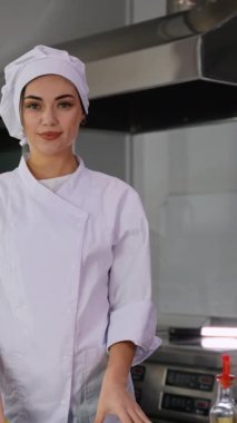Beyaz üniformalı kendinden emin bir kadın şef modern bir mutfakta duruyor ve taze malzemelerle lezzetli bir yemek hazırlıyor..