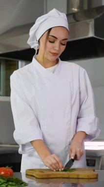 Şefin elleri beyaz bir üniformayla profesyonel bir mutfakta ahşap bir kesme tahtasındaki taze yeşil otları keserken..