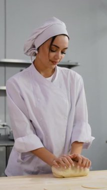 Beyaz üniformalı bir kadın şef, profesyonel bir mutfakta ahşap bir masaya hamur yoğurur. Pişirmeye ya da pişirmeye hazırlanır..
