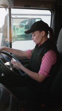 Kulübede oturan kadın kamyon şoförü, yolculuğuna başlamadan önce rotayı incelemek için akıllı telefonunda GPS navigatörü kullanıyor..