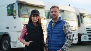 Erkek ve kadın kamyon şoförleri, bir sonraki teslimat görevleri için kendinden emin ve hazır bir şekilde bir kamyon otoparkında yan yana duruyorlar..
