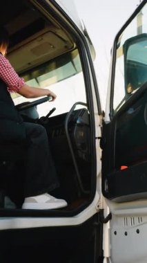 Kadın kamyon şoförü, elinde direksiyon olan beyaz bir kamyonun taksisinde oturuyor ve bir yolculuğa hazırlanıyor. Taşımacılık ve ulaşıma odaklan.