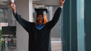 Heyecanlı Afro-Amerikan bayan mezun, kep ve cübbe giyerek, diploma tutarken ellerini kaldırarak, akademik başarısını neşeyle kutluyor..