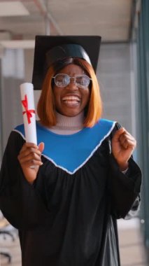 Heyecanlı Afro-Amerikan bayan mezun, kep ve cübbe giyerek, diploma tutarken ellerini kaldırarak, akademik başarısını neşeyle kutluyor..