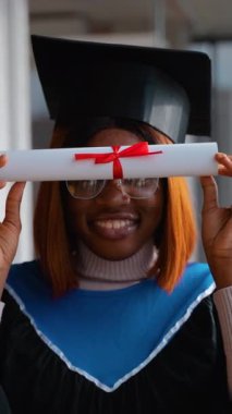 Siyah kep ve mavi kuşaklı bir cübbe giyen Afro-Amerikan mezunu. Eğitimini tamamladıktan sonra gururlu ve kendinden emin bir ifadeyle içeride duruyor..