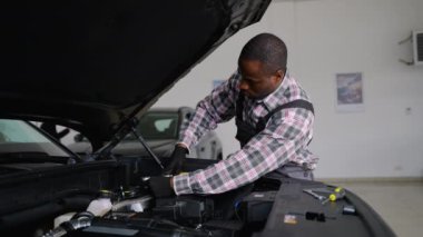 Profesyonel bir oto tamircisi eldiven giyer ve tulum giyer atölyede bir araba motorunu tamir eder, bakım ve teşhislere odaklanır.