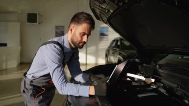 Bir atölyede çalışan profesyonel bir oto tamircisi, verimli araç bakımı ve sorun giderme garantisi veren bir dizüstü bilgisayardaki motor tanılarını dikkatle inceler..