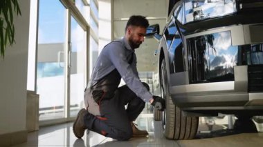 Profesyonel bir tamirci modern bir atölyede araba tekerleğini sıkarken diz çöker ve düzgün bir bakım ve araç güvenliği sağlar..