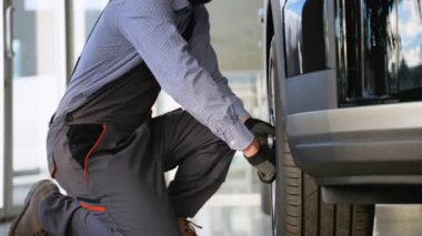 Modern bir SUV 'nin tekerlek fındıklarını sıkarken bir oto tamircisinin diz çöktüğü yakın plan..