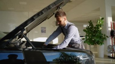 Yetenekli bir oto tamircisi modern, iyi ışıklandırılmış bir araç hizmet merkezinde açık kaputun altındaki bir araba motorunu kontrol eder ve tamir eder..