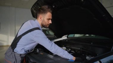 Profesyonel bir otomobil tamircisi modern bir cipin motorunu iyi aydınlatılmış bir garajda inceleyerek rutin bir araç teftişi yapıyor..