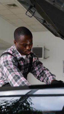 Tulum ve eldiven giyen bir oto tamircisi, iyi aydınlatılmış bir atölyede, bakım, teşhis ve araç servisine odaklanan bir araba motorunu tamir eder..